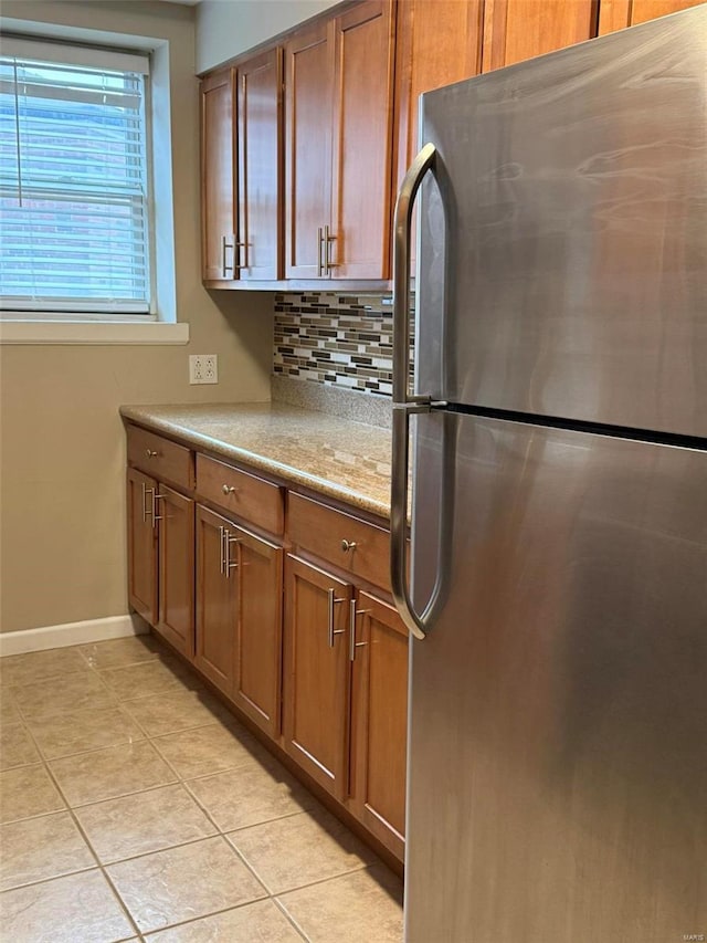 kitchen with light tile patterned floors, brown cabinetry, tasteful backsplash, and freestanding refrigerator