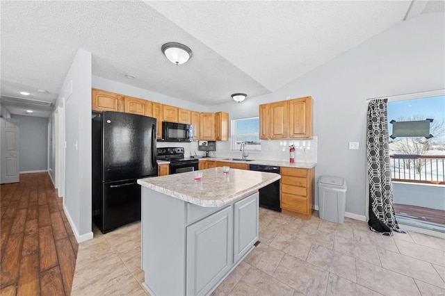 kitchen with lofted ceiling, a center island, light countertops, black appliances, and a sink