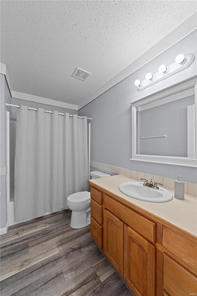 bathroom with a textured ceiling, wood finished floors, vanity, visible vents, and shower / bath combo