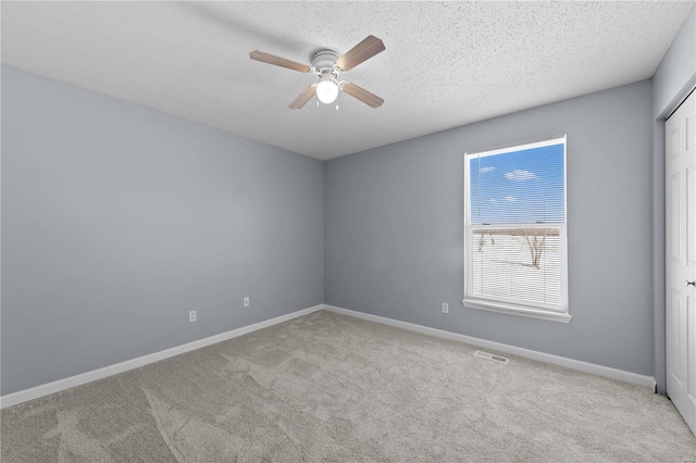 empty room with baseboards, visible vents, a ceiling fan, light colored carpet, and a textured ceiling