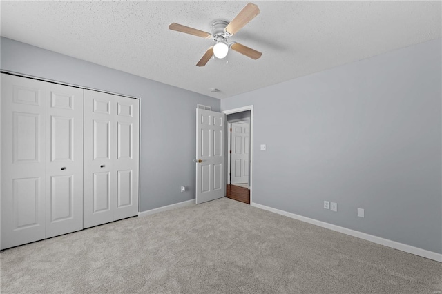 unfurnished bedroom featuring light carpet, baseboards, ceiling fan, a textured ceiling, and a closet