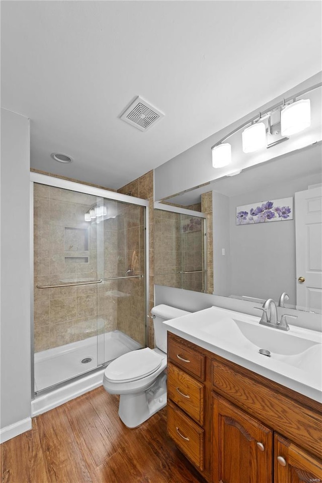 bathroom with toilet, wood finished floors, vanity, visible vents, and a stall shower