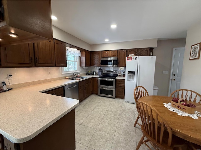 kitchen with dark brown cabinetry, appliances with stainless steel finishes, a sink, light countertops, and backsplash