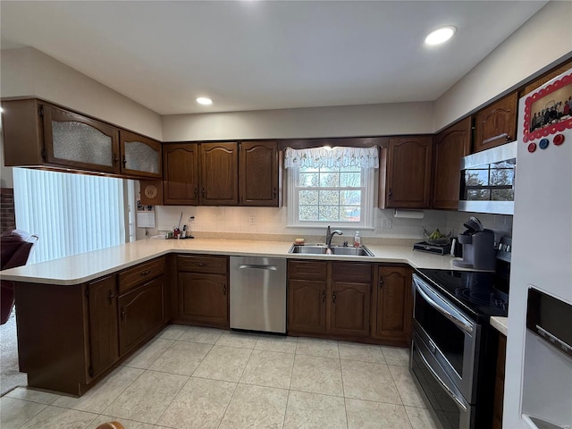 kitchen with light countertops, appliances with stainless steel finishes, a sink, dark brown cabinetry, and a peninsula