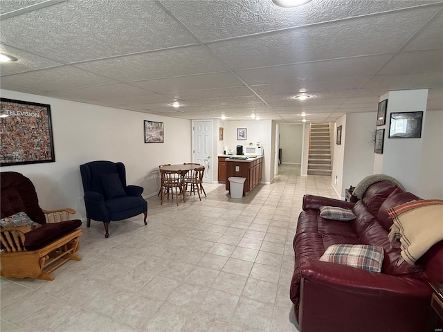 living area featuring baseboards, stairway, and a drop ceiling