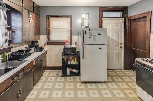 kitchen featuring dark brown cabinetry, white appliances, a sink, light countertops, and light floors