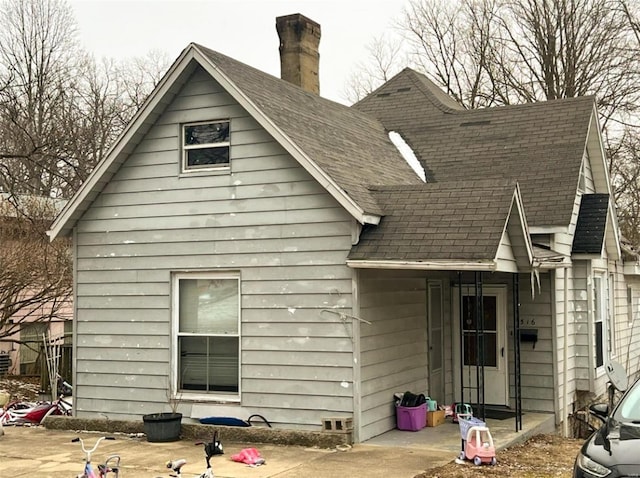 back of house with a chimney and a shingled roof