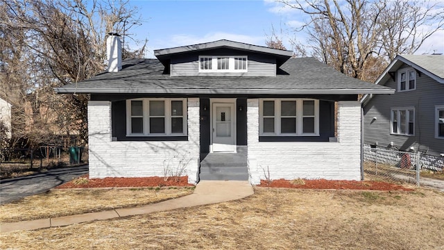 bungalow-style house with stone siding, roof with shingles, a chimney, and fence