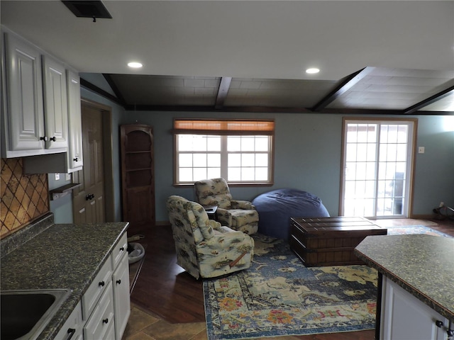 kitchen with decorative backsplash, open floor plan, beamed ceiling, white cabinetry, and a sink