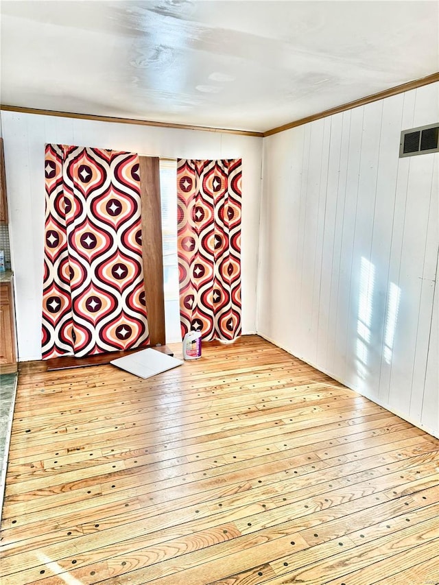 spare room featuring crown molding, wooden walls, visible vents, and light wood-style floors