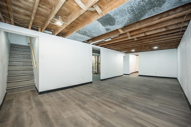 finished below grade area featuring stairs, dark wood-type flooring, and baseboards