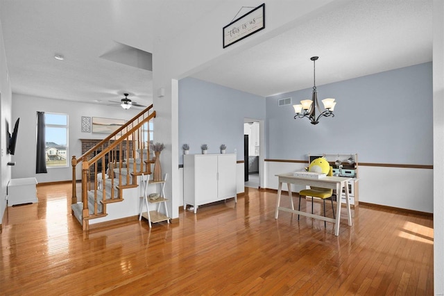 dining space with baseboards, visible vents, wood-type flooring, stairs, and ceiling fan with notable chandelier