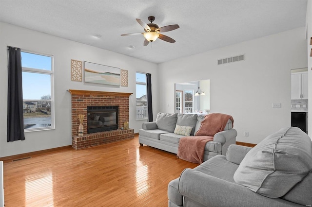 living room with light wood-style floors, visible vents, a fireplace, and a ceiling fan