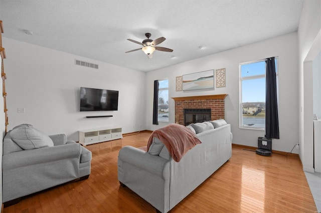 living area featuring a brick fireplace, visible vents, light wood finished floors, and a ceiling fan