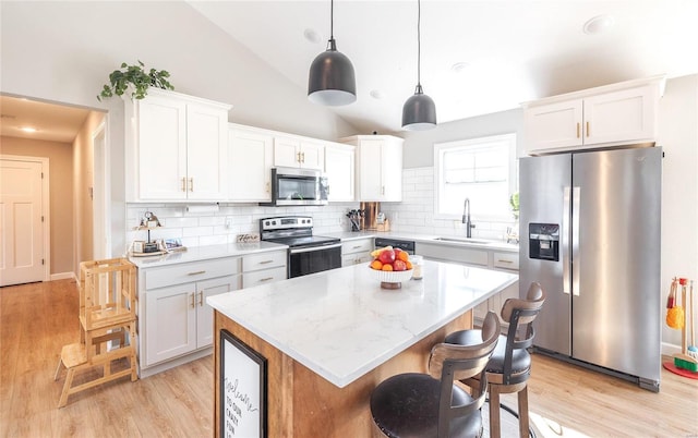 kitchen with a center island, appliances with stainless steel finishes, white cabinets, vaulted ceiling, and a sink