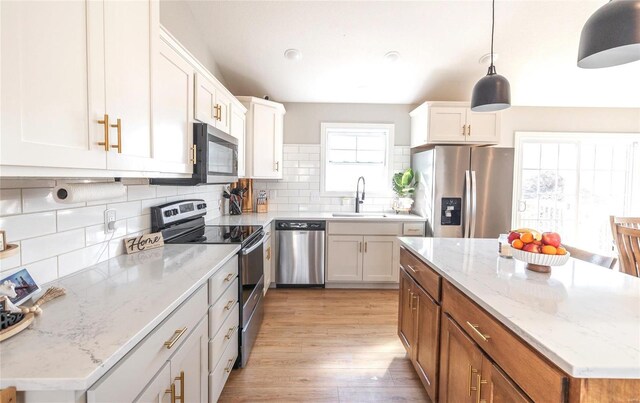 kitchen featuring light wood-style flooring, a sink, appliances with stainless steel finishes, decorative backsplash, and brown cabinetry