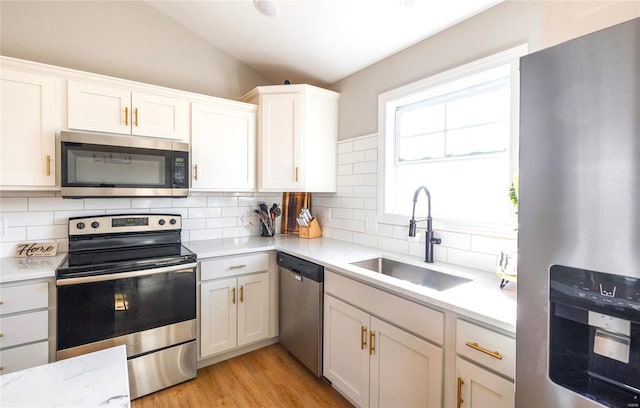 kitchen featuring light wood-style flooring, a sink, vaulted ceiling, appliances with stainless steel finishes, and decorative backsplash