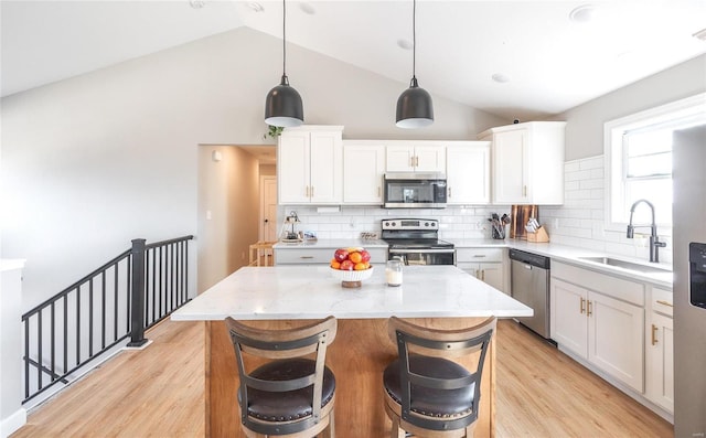 kitchen featuring light stone counters, light wood finished floors, stainless steel appliances, white cabinets, and a sink