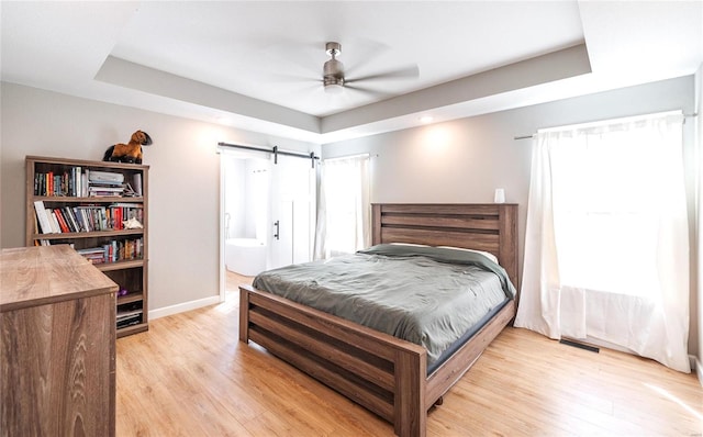 bedroom featuring light wood-style floors, a barn door, multiple windows, and a tray ceiling