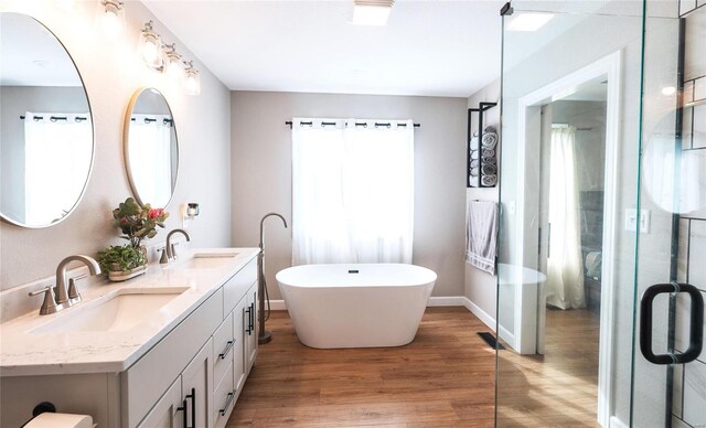 bathroom with double vanity, wood finished floors, a freestanding tub, and a sink