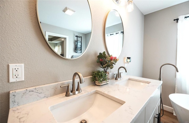 full bath featuring double vanity, visible vents, a sink, and a textured wall