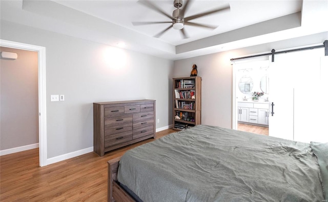 bedroom with a barn door, baseboards, a raised ceiling, and wood finished floors