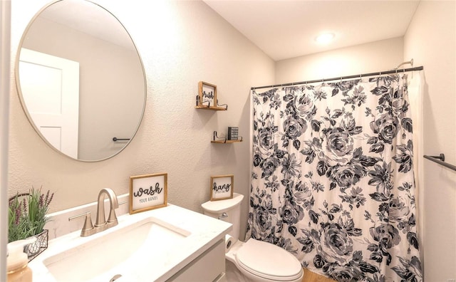 bathroom with toilet, a textured wall, a shower with shower curtain, and vanity