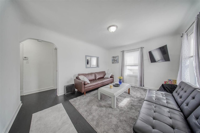 living room with baseboards, visible vents, arched walkways, and a wealth of natural light