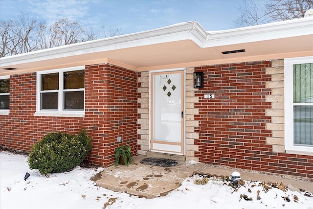 snow covered property entrance featuring brick siding