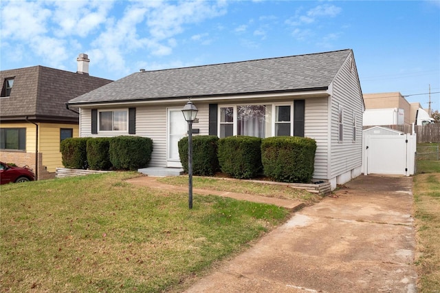 view of front facade featuring a shingled roof, a front lawn, fence, and a gate