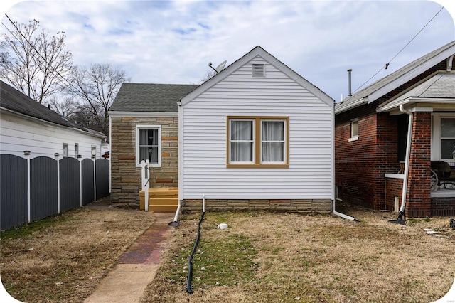 bungalow-style home featuring a shingled roof, stone siding, fence, and a front lawn