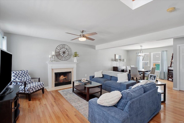 living room with ceiling fan with notable chandelier, light wood finished floors, a fireplace, and baseboards