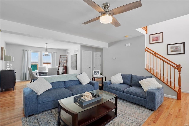 living room featuring baseboards, visible vents, ceiling fan, stairway, and wood finished floors