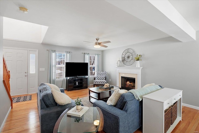 living area featuring baseboards, light wood-style flooring, a premium fireplace, stairway, and ceiling fan