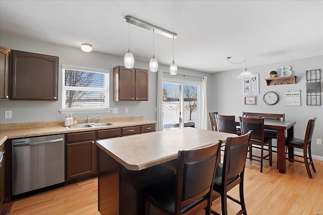 kitchen with a kitchen island, light countertops, dark brown cabinets, stainless steel dishwasher, and a sink