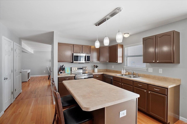 kitchen featuring stainless steel appliances, a sink, a kitchen island, hanging light fixtures, and light countertops