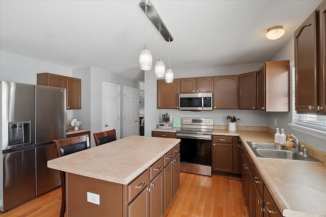 kitchen with stainless steel appliances, a sink, light countertops, a center island, and light wood finished floors