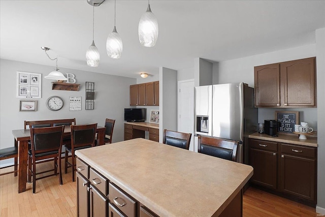 kitchen featuring a kitchen island, light countertops, hanging light fixtures, and stainless steel fridge with ice dispenser