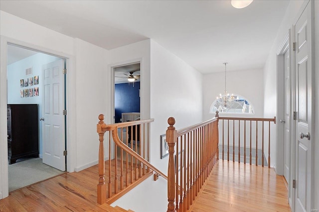 hallway with light wood-style flooring, visible vents, a chandelier, and an upstairs landing