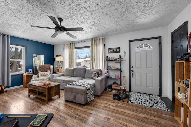 living room featuring ceiling fan, a textured ceiling, baseboards, and wood finished floors