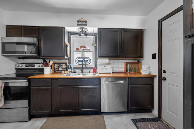 kitchen featuring decorative backsplash, butcher block counters, stainless steel appliances, dark brown cabinets, and a sink