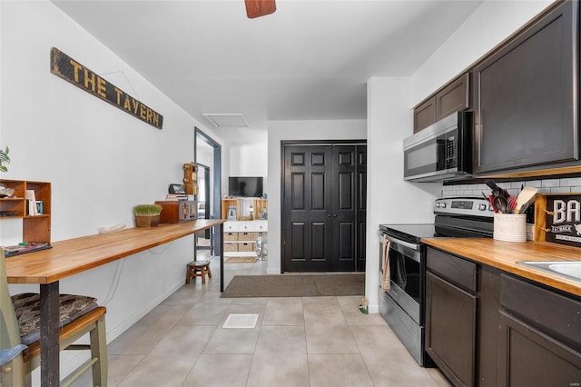 kitchen featuring dark brown cabinetry, tasteful backsplash, light tile patterned floors, stainless steel appliances, and wooden counters