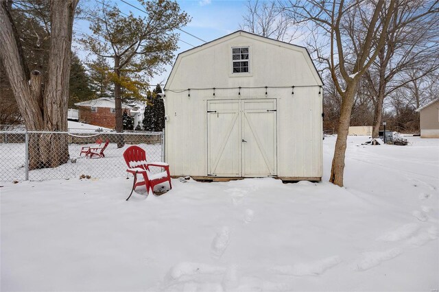 snow covered structure with an outbuilding, fence, and a storage unit