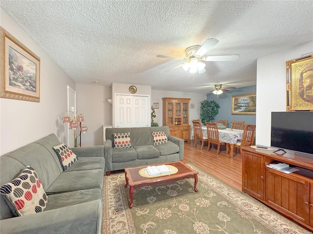 living room featuring ceiling fan, light wood-style flooring, and a textured ceiling