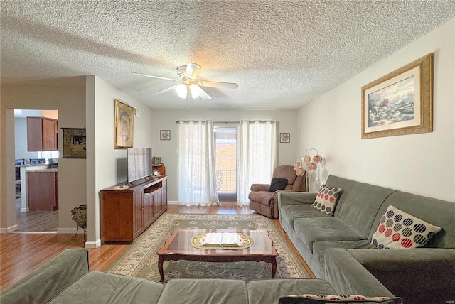 living area featuring light wood-style flooring, ceiling fan, and a textured ceiling