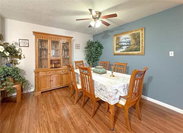 dining space with a ceiling fan, baseboards, light wood-style flooring, and a textured ceiling