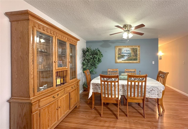 dining space featuring a textured ceiling, light wood-type flooring, a ceiling fan, and baseboards