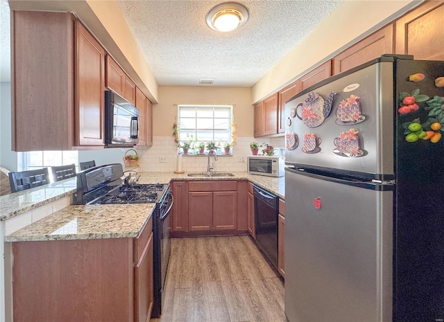 kitchen featuring a sink, light wood-type flooring, decorative backsplash, light stone countertops, and black appliances