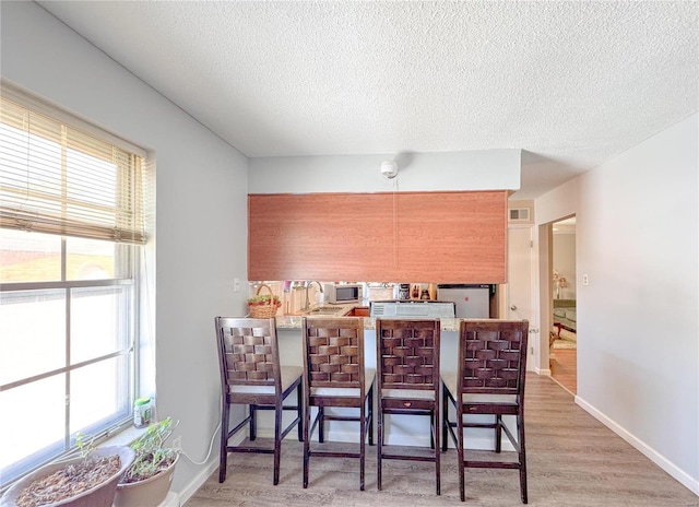 kitchen featuring baseboards, light wood-style flooring, a kitchen breakfast bar, a peninsula, and a textured ceiling