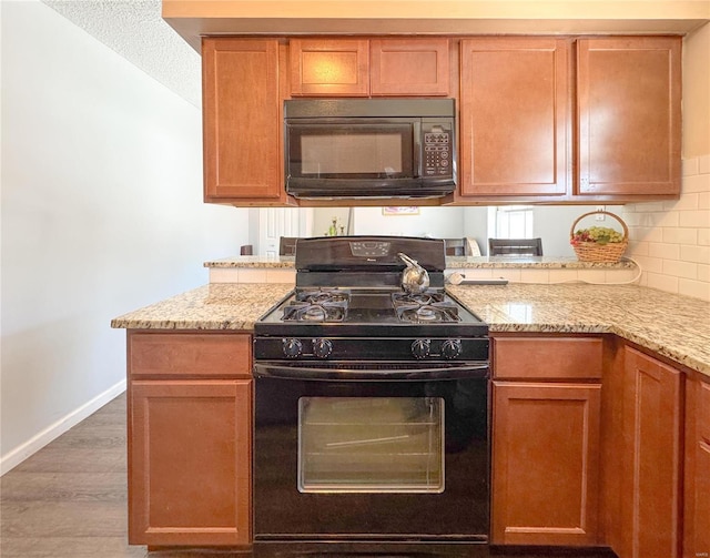 kitchen with baseboards, light stone counters, wood finished floors, black appliances, and backsplash